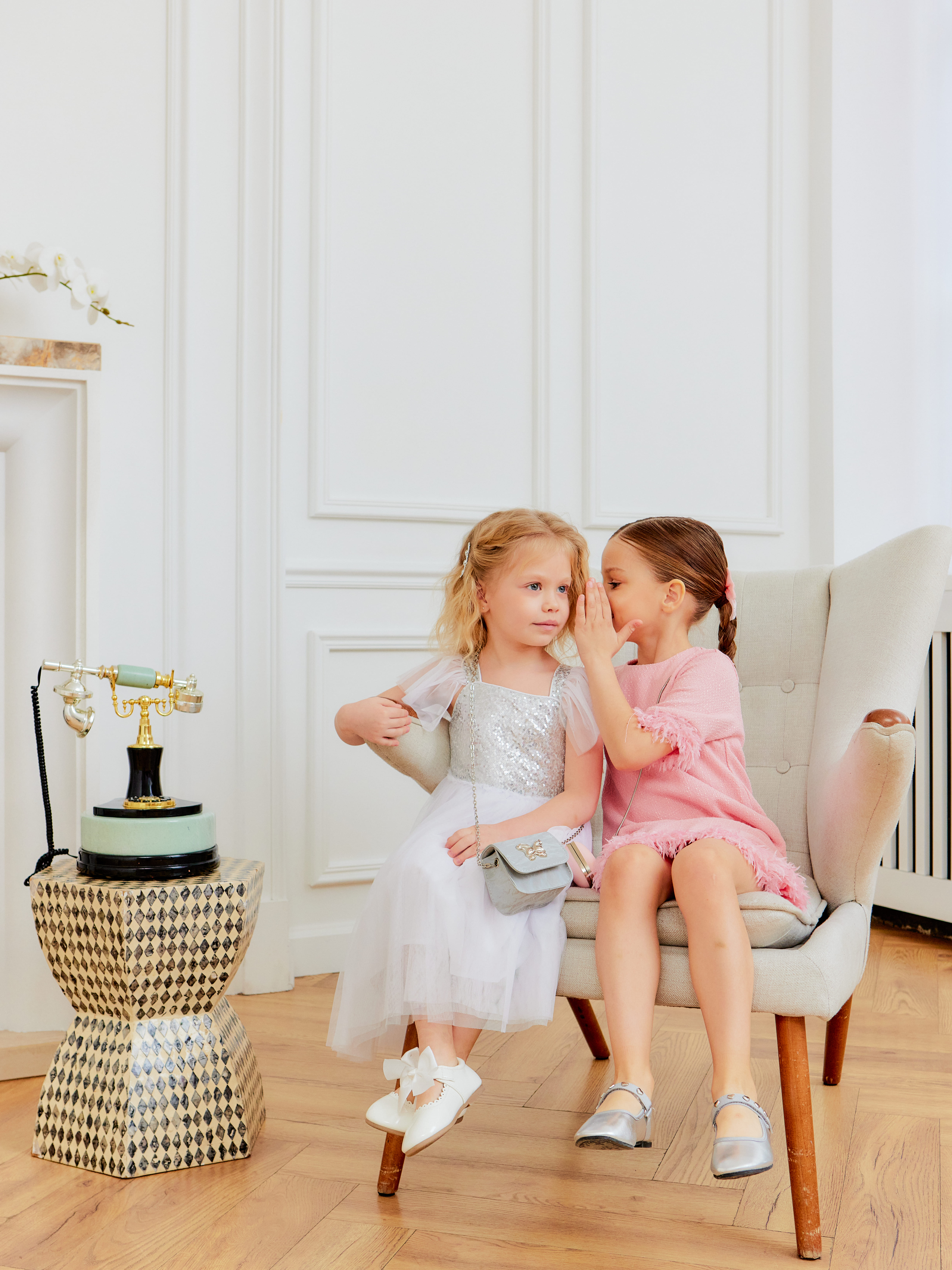 Девочки в нарядных платьях сидят на стуле